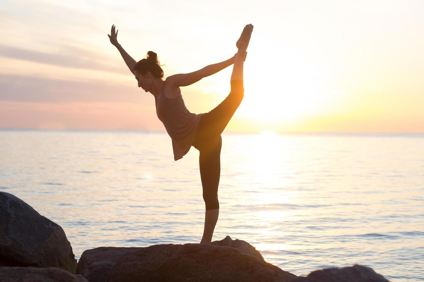 fitness mixed race asian woman in yoga pose on the morning beach, beautiful fit woman practice fitness exrxise stones, morning sea or ocean background photo