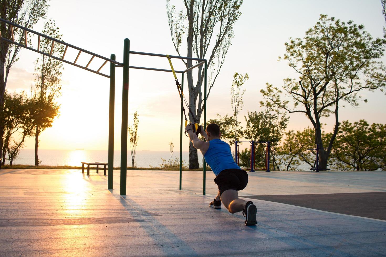 workout with suspension straps In the outdoor gym, strong man training early in morning on the park, sunrise or sunset in the sea background photo