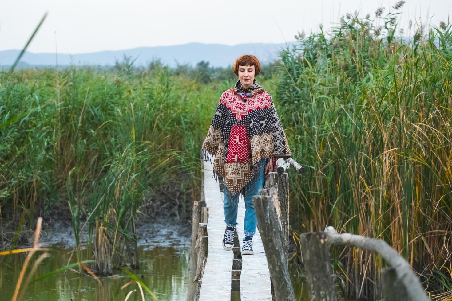 una joven viajera vestida con un poncho camina al aire libre en los campos de otoño foto