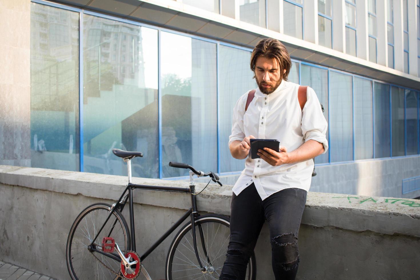 Young bearded man with leather backpack walking with black bicycle photo