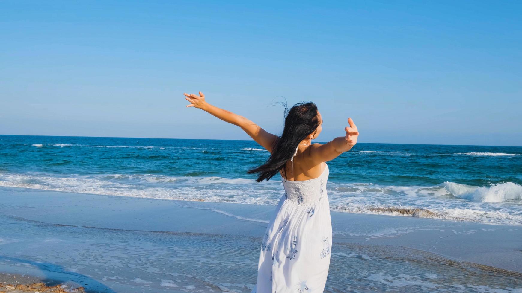 Young beautiful woman dressed in a white dress walk barefoot on the summer beach photo