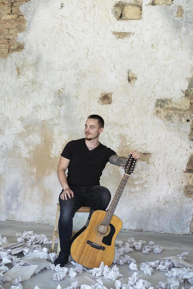 joven con guitarra en una habitación vacía, músico y compositor solo en el estudio foto