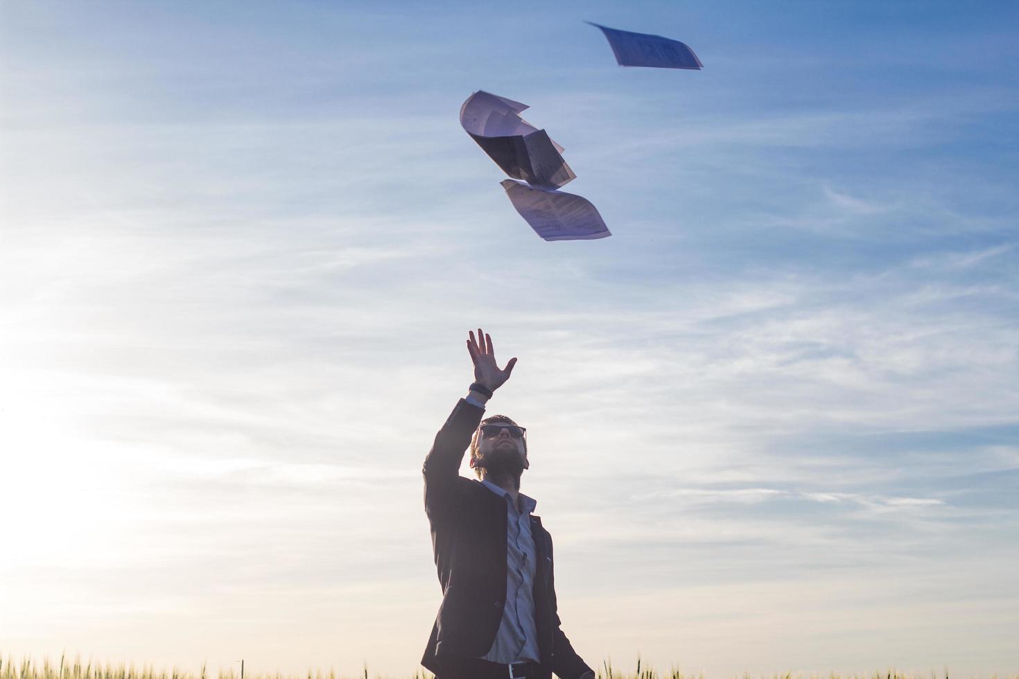 retrato de un joven hombre de negocios lanzando hojas de papel al aire, puesta de sol en el fondo de los campos de verano foto