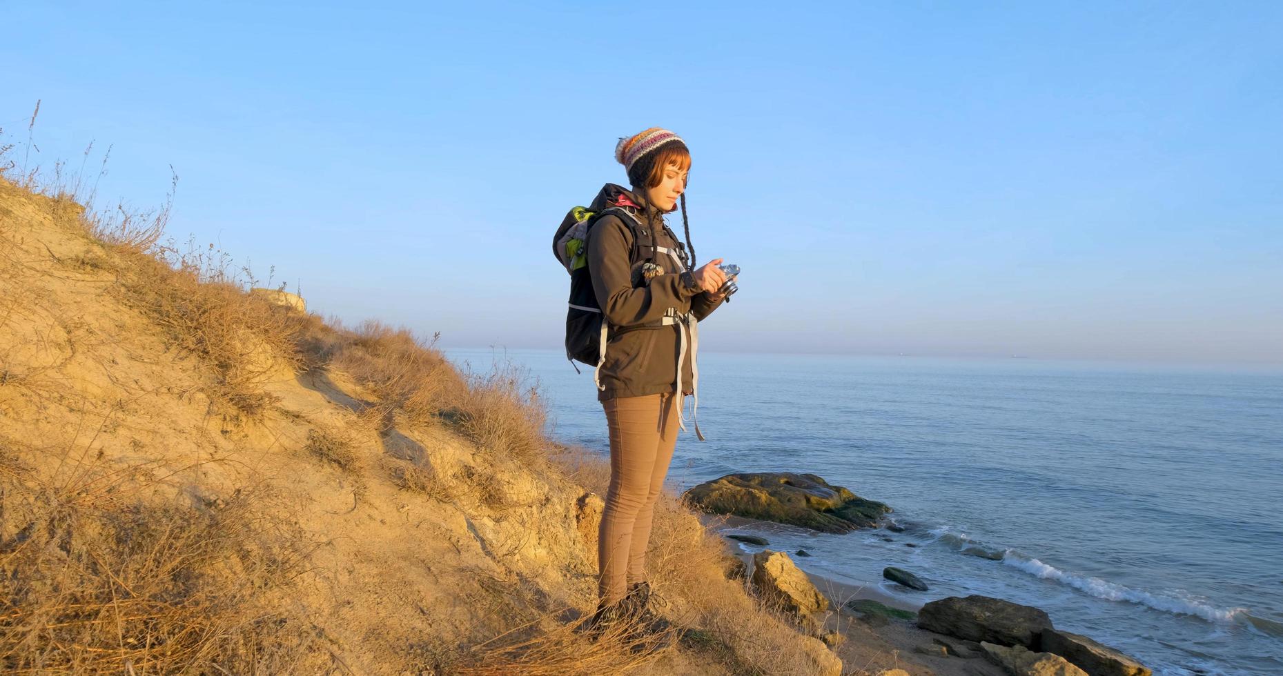 joven viajera con mochila y cámara de cine retro viaja en las montañas de otoño cerca del mar foto