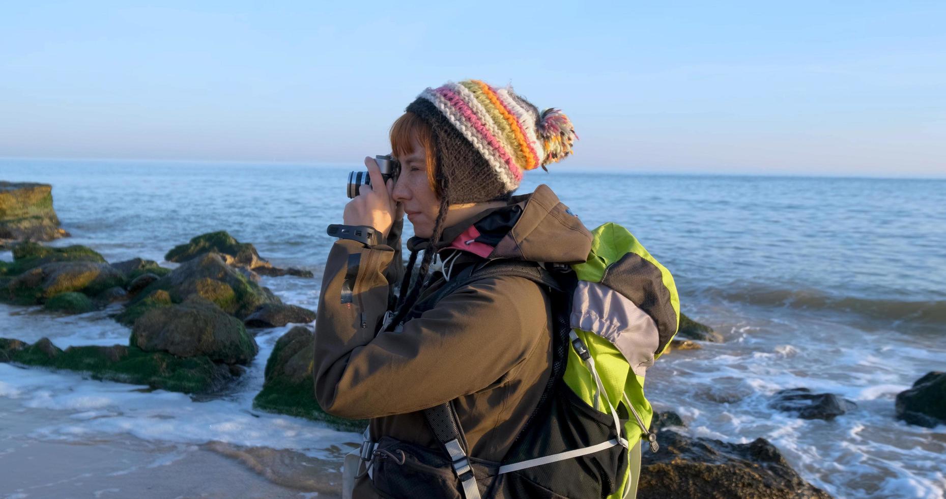 joven viajera con mochila y cámara de cine retro viaja en las montañas de otoño cerca del mar foto