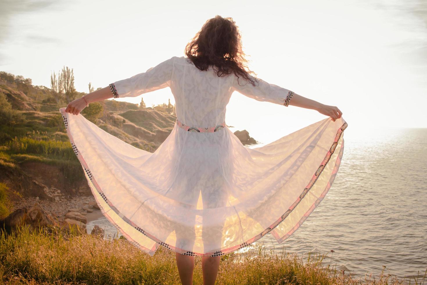 young woman walking on the morning beach in beautiful white dress. Fit female having good time during turing the sunrise. photo