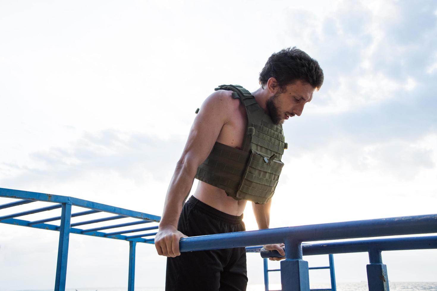 joven atleta barbudo entrenando al aire libre con chaleco ponderado, ejercicio con portador de placa militar foto