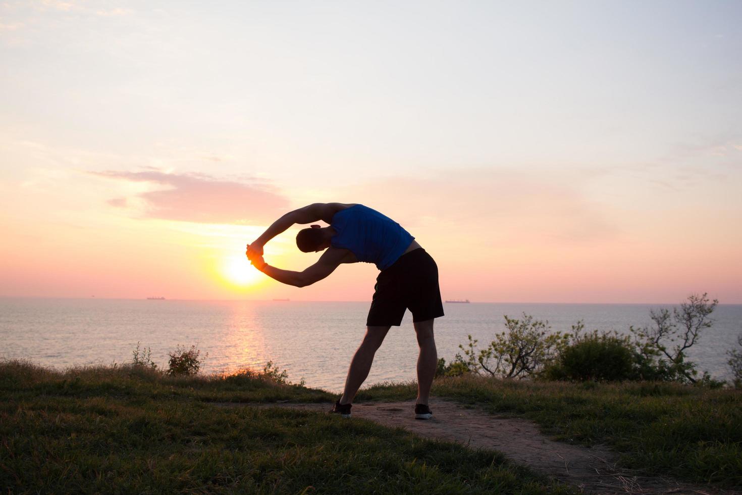 Happy fit runner watching sunrise or sunset with rised fists, young athlete on grass during the sunrise in the sea photo