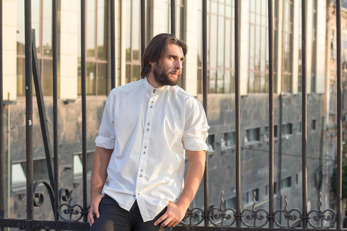 retrato de hombre barbudo con camisa blanca, fondo urbano, hipster posando en el puente foto