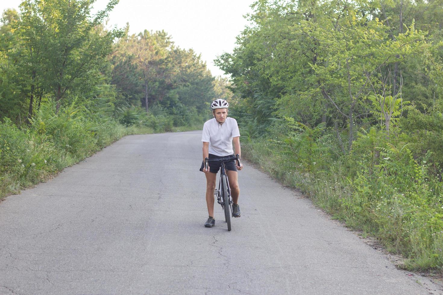 retrato de un joven ciclista parado solo en la carretera en el bosque foto