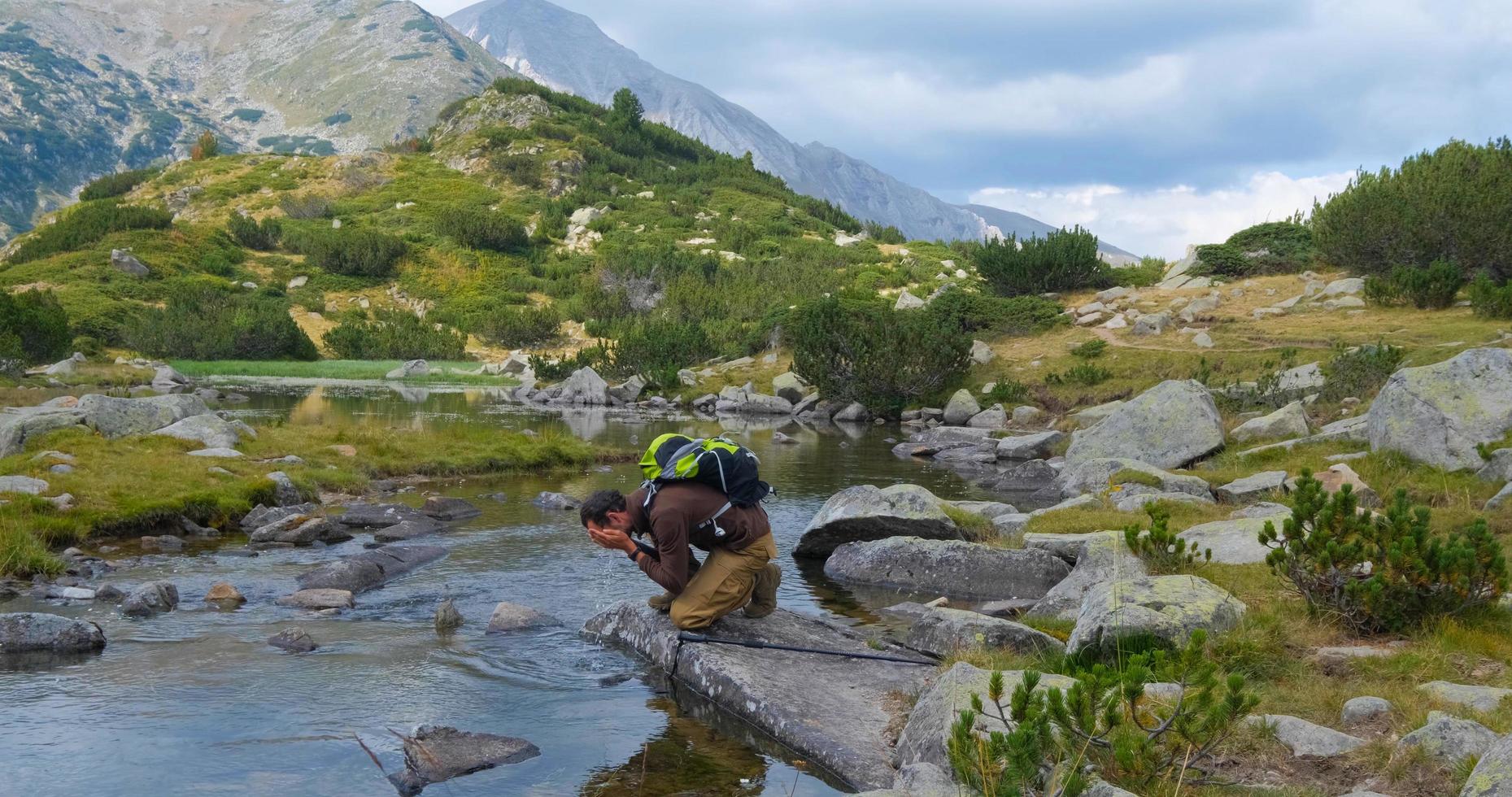 Yong male traveler in the mountains sitting near river photo