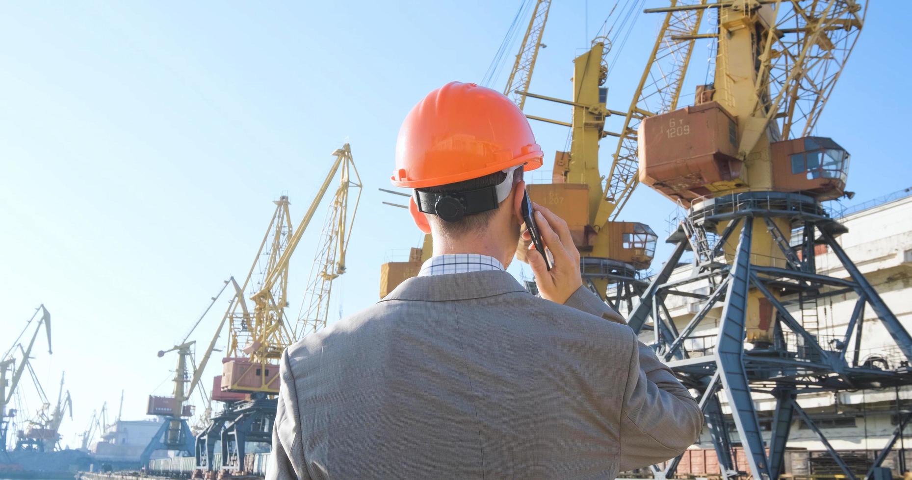 Young male worker of sea harbor in helmet, cargo manager in suit and halmet works outdoor , cranes and sea background photo