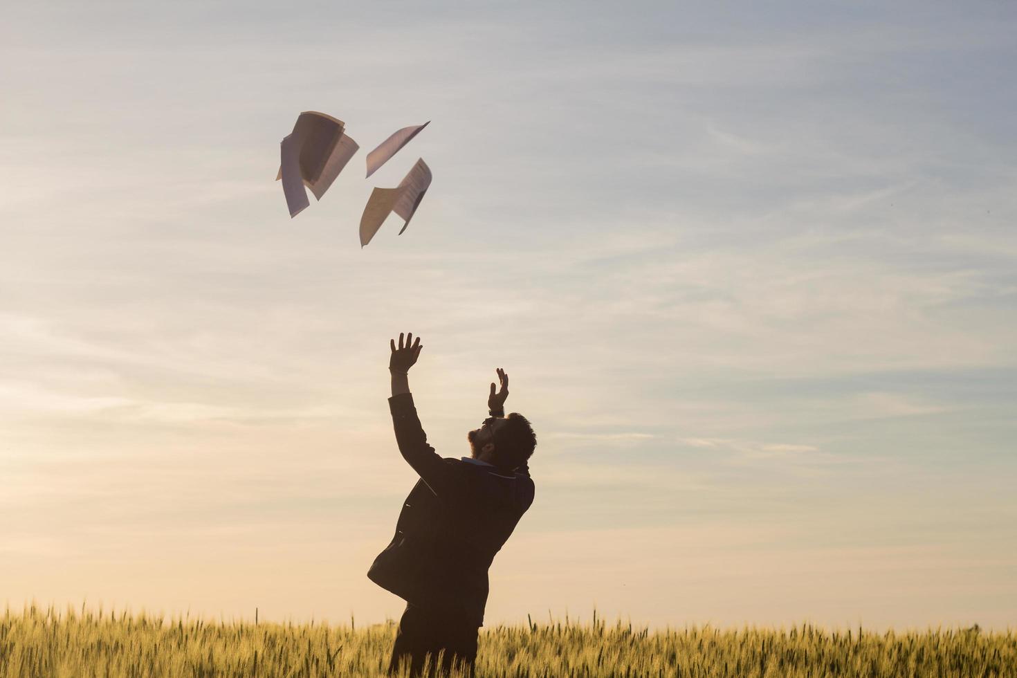 retrato de un joven hombre de negocios lanzando hojas de papel al aire, puesta de sol en el fondo de los campos de verano foto