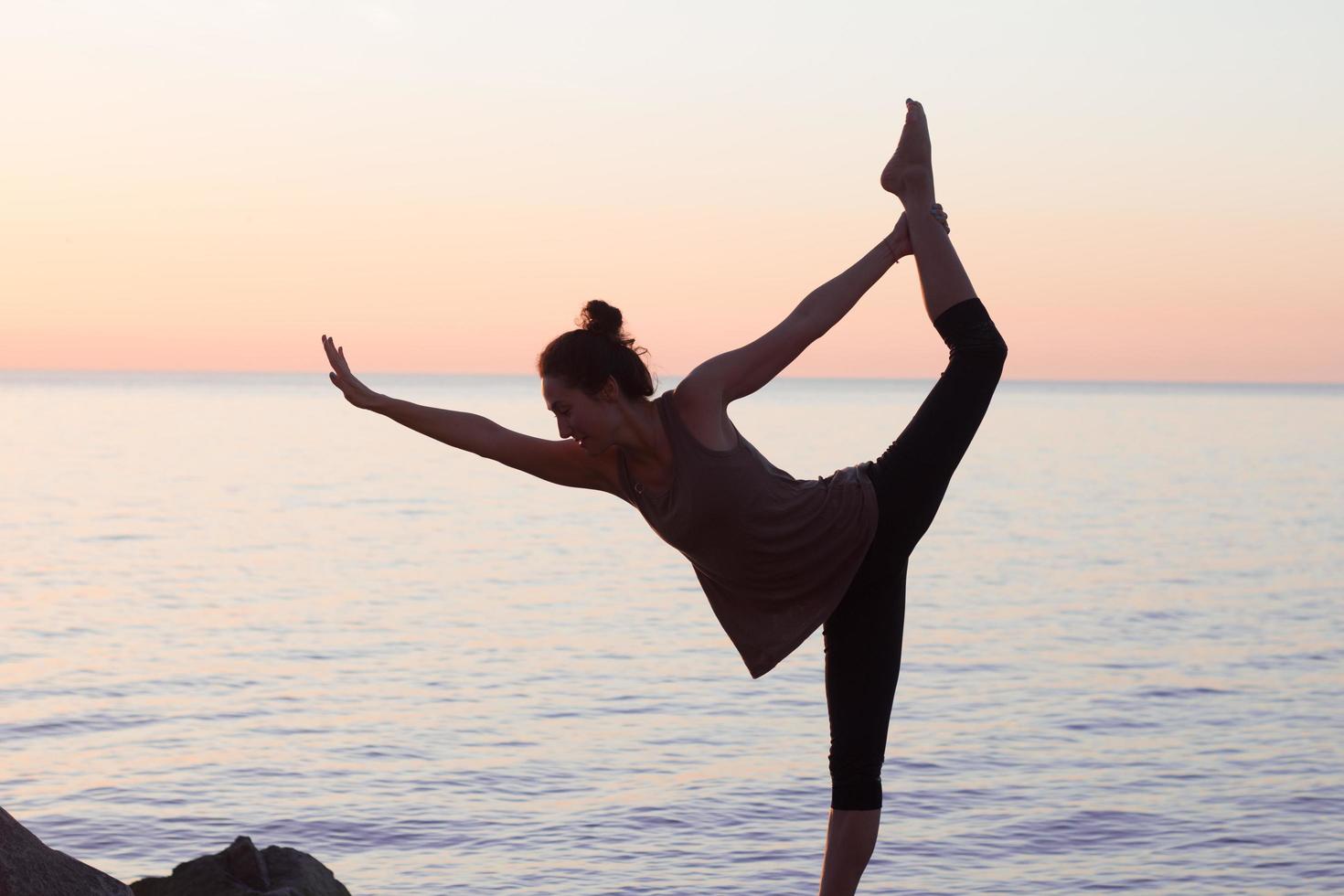 fitness mixed race asian woman in yoga pose on the morning beach, beautiful fit woman practice fitness exrxise stones, morning sea or ocean background photo