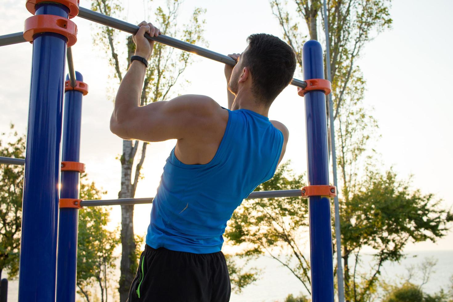 Muscular man doing pull-ups on horizontal bar, training of strongman on outdoor park gym in the morning. photo