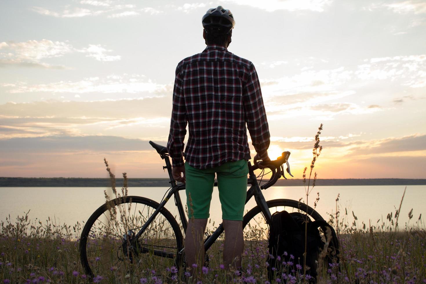 silhouette of a man with touring road bike watching and make photo of sunset in lake on cellphone