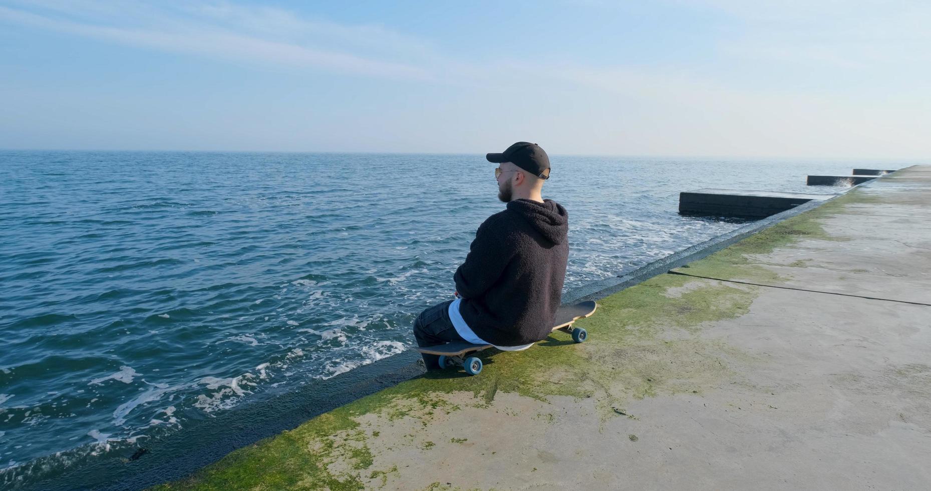 Young male with skateboard relaxing near sea photo