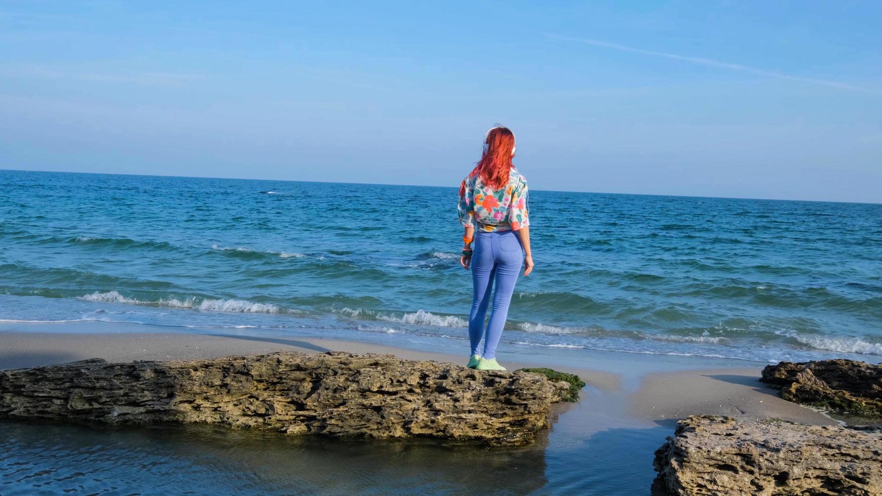 mujer joven con cabello colorido camina en la playa de verano y escucha música con auriculares foto