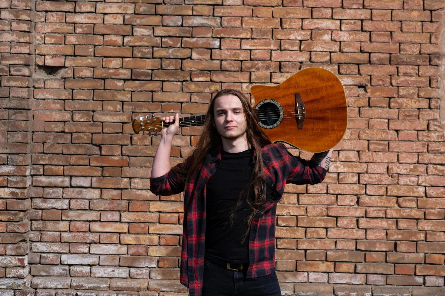 Young male with long hair and tattoo play on acoustic guitar outdoors on the street photo