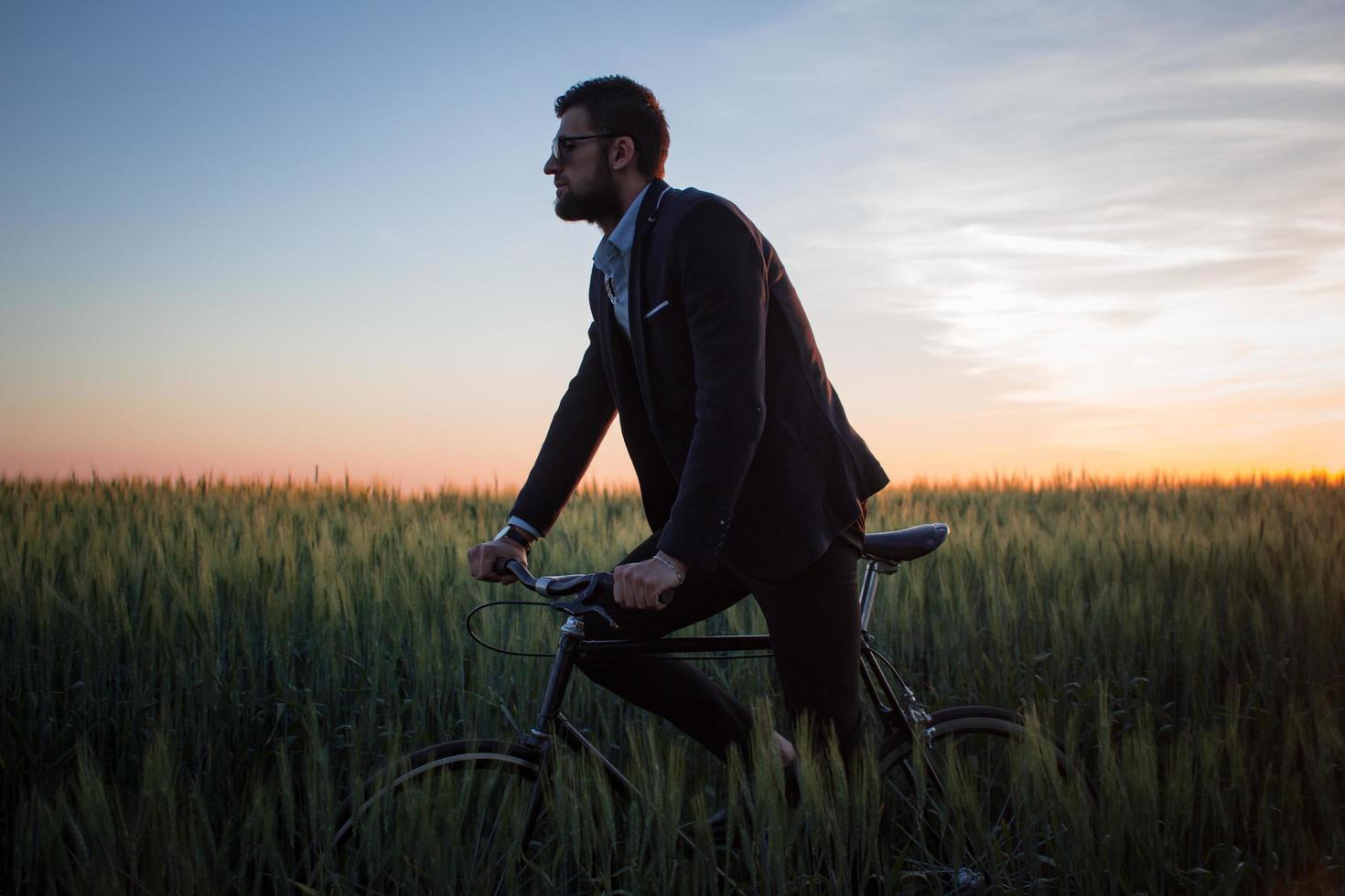 A caucasian businessman riding a bicycle in summer fields, Male in business suit ride on fixie bike. photo