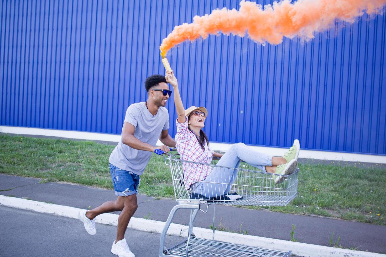 Happy young couple riding on trolley on empty mall parking , hipster friend have good time during shopping, couple in love riding on shopping cart photo