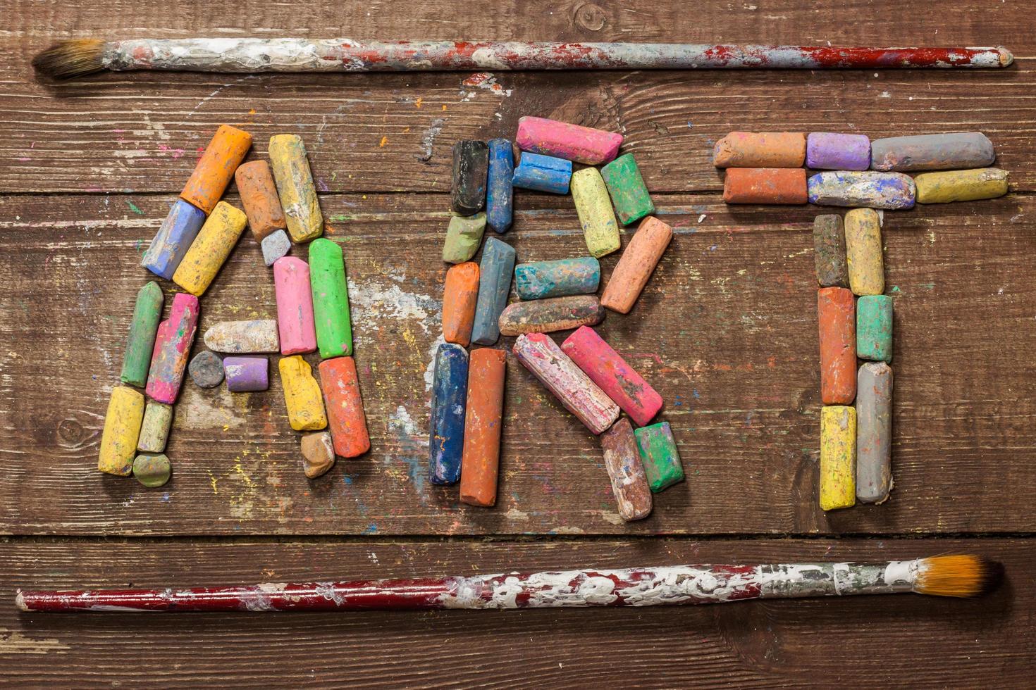 Piece of chalk with pain brushes on wooden table photo