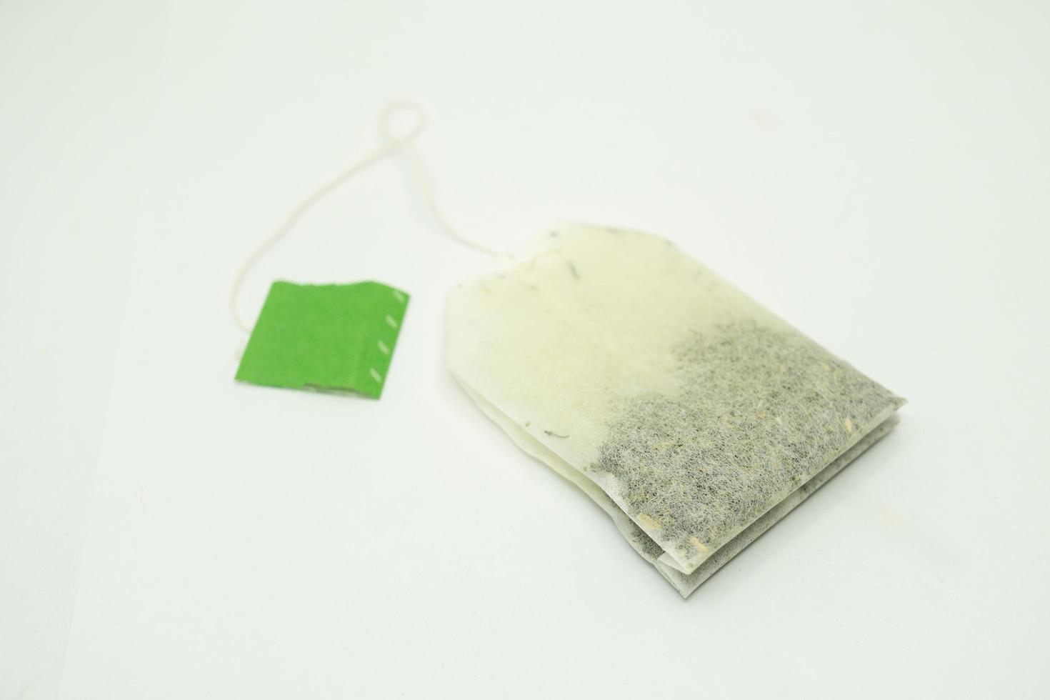 Teabag with green label. Isolated on white background. Close-up of tea bag. photo