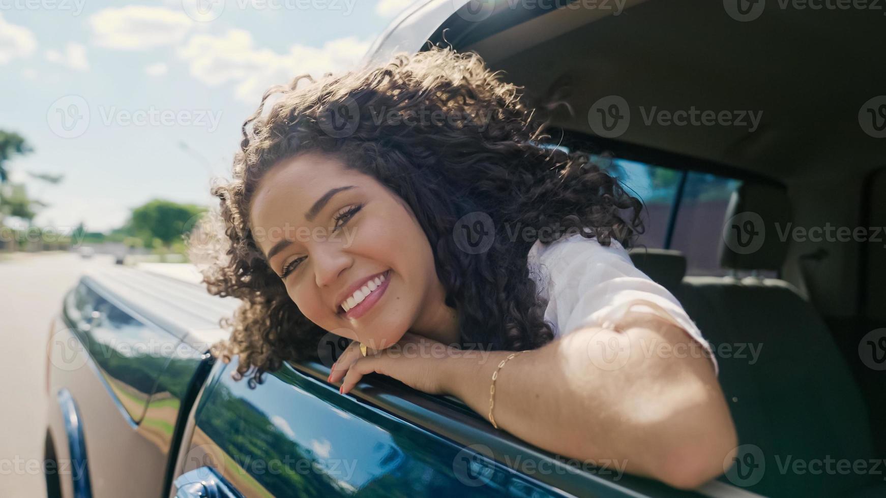 Latin woman in car window. Car trip. Curly hair in wind. Girl looks out of car window. photo