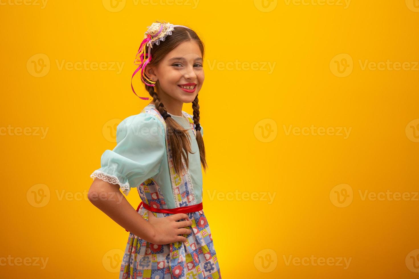 Child in typical clothes of famous Brazilian party called Festa Junina in celebration of Sao Joao. Beautiful girl on yellow background. photo