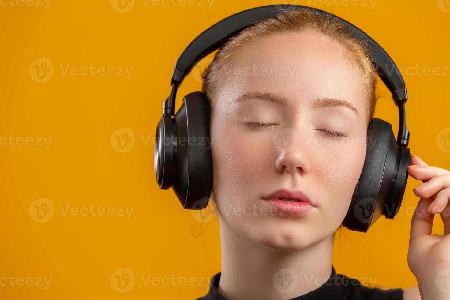 Happy and carefree excited redhead hipster girl like her new headphones, dancing with hands lifted up and smiling enjoy listening music over orange background, boost mood with favorite song. photo