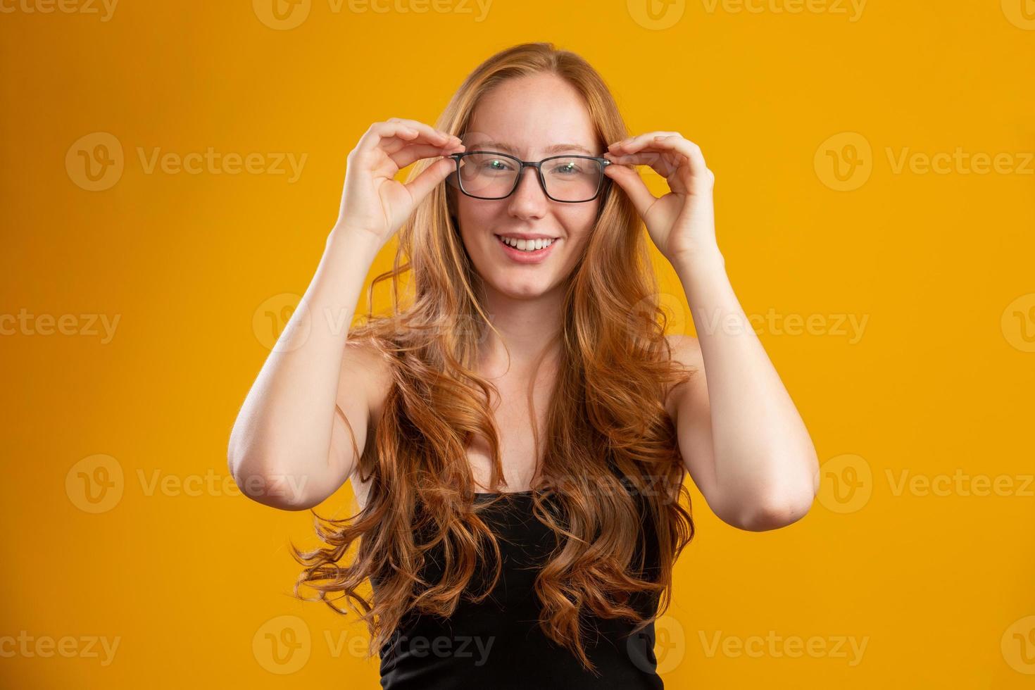 Beautiful young redhead woman with curly hair happy with her glasses. Eye care concept. On yellow background. photo