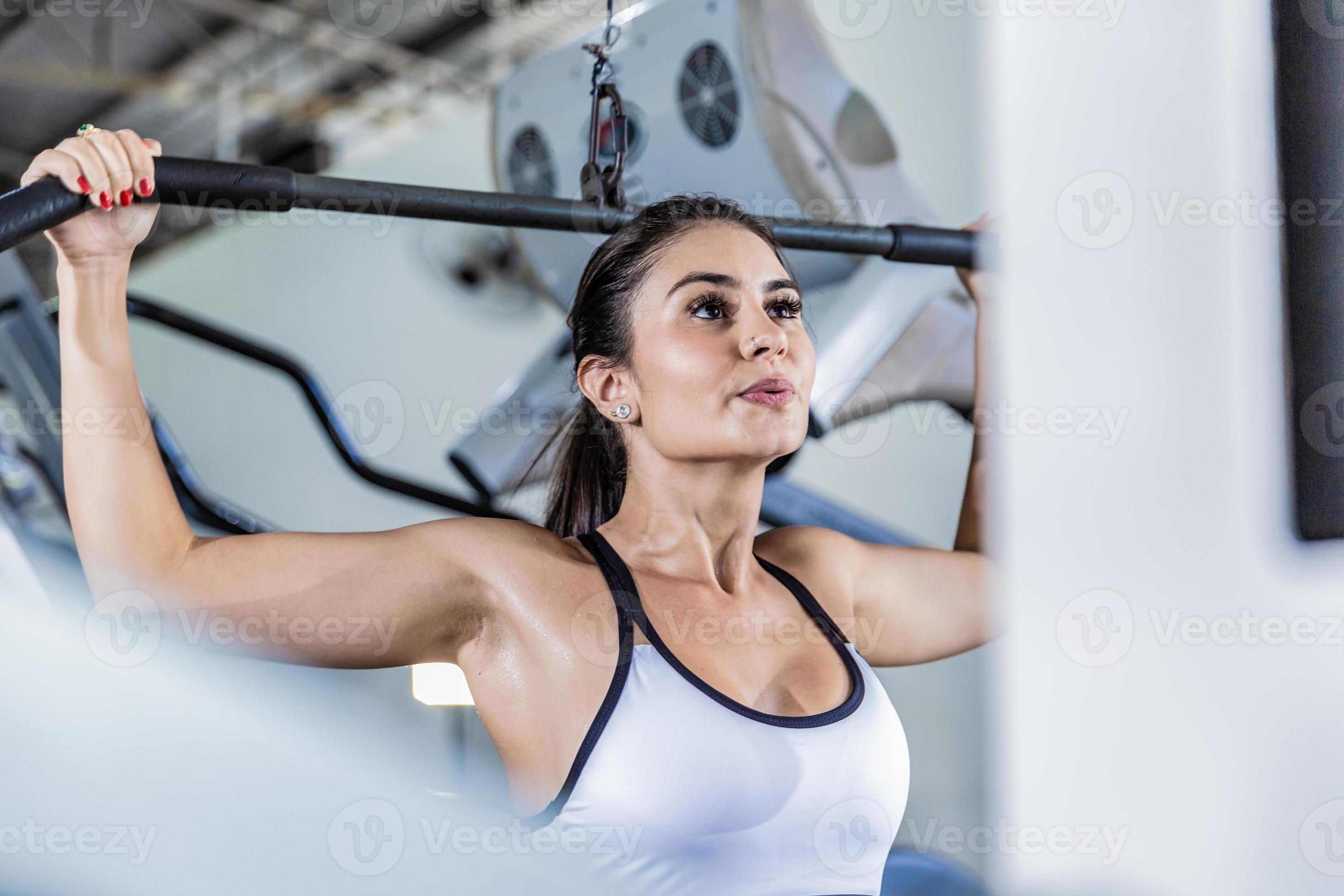 Athletic woman using machine for pumping back muscles in gym