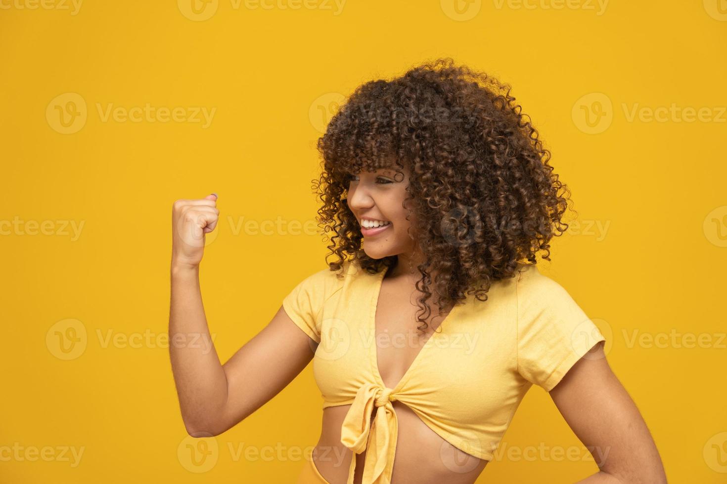 Young beautiful brunette curly hair girl happily rejoicing saying yes on yellow background. Success and achievement concept. Cheerful pretty woman on yellow background. photo