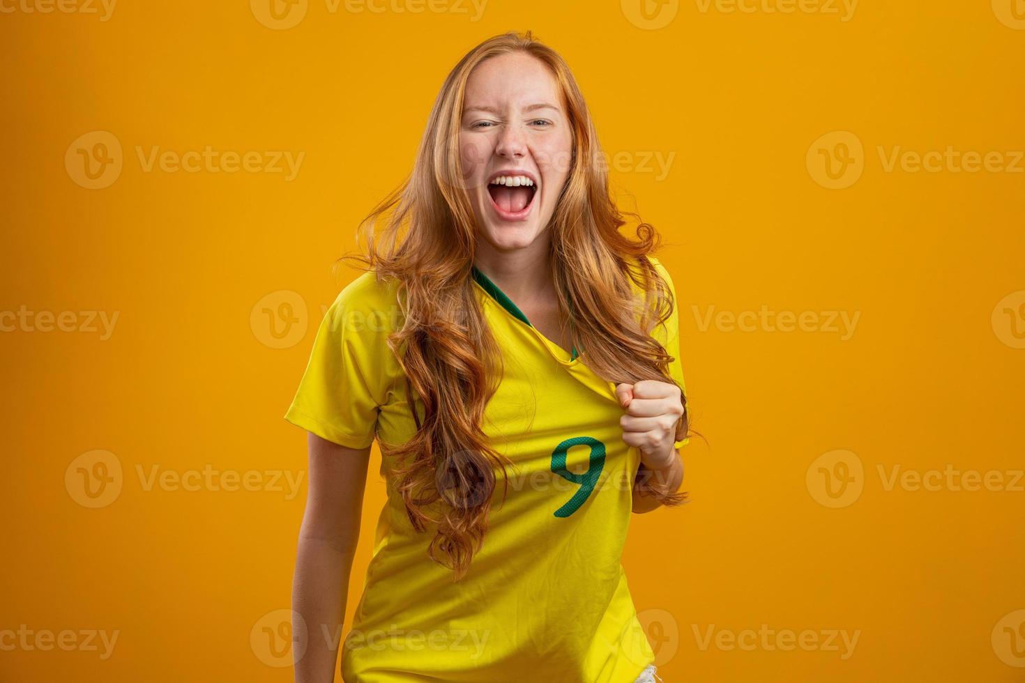 partidario de brasil. hincha brasileña pelirroja celebrando el fútbol, partido de fútbol con fondo amarillo. colores de brasil. foto