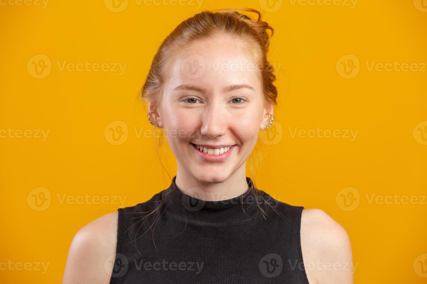 retrato de una hermosa y alegre pelirroja sonriendo riéndose mirando la cámara sobre un fondo amarillo. foto