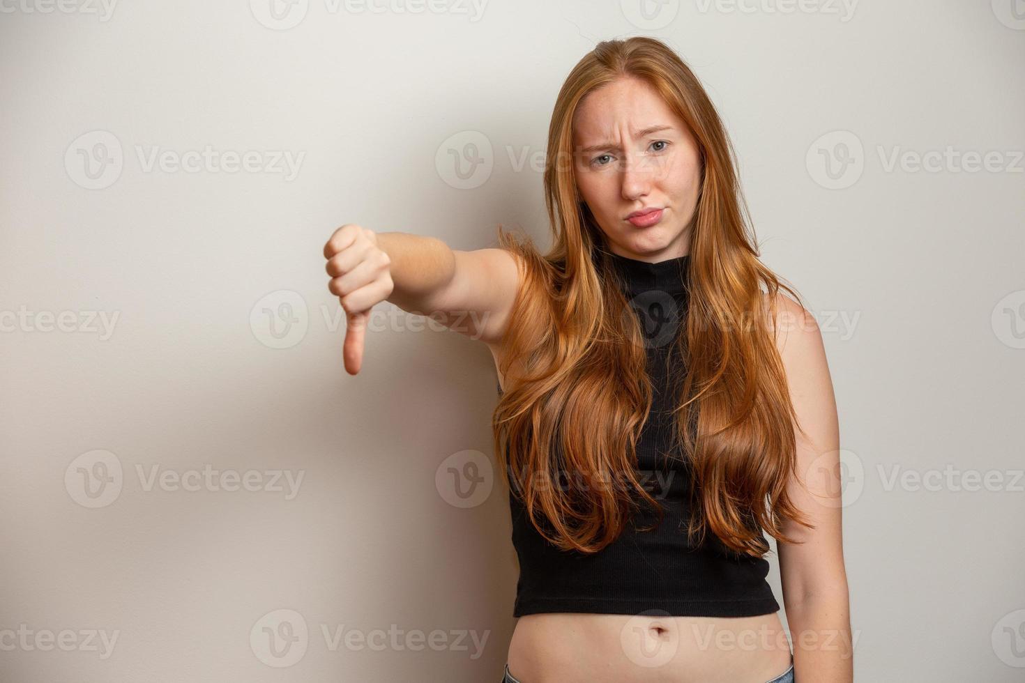 Unhappy redhead woman giving thumbs down gesture looking with negative expression and disapproval. Yellow background. photo