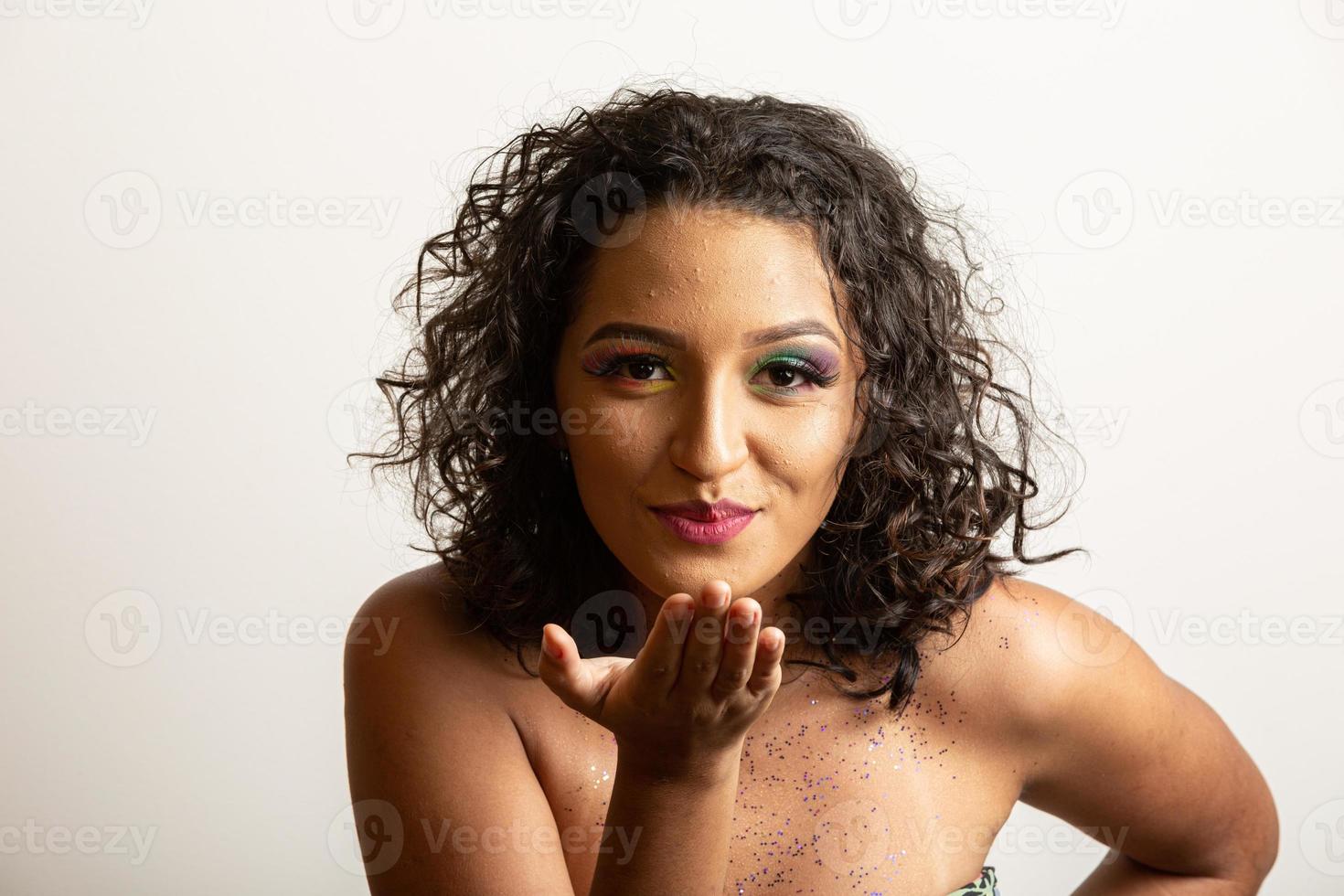 vamos a la chica fiestera que sopla confeti contra el fondo blanco. mujer joven feliz divirtiéndose en el carnaval. concepto de vacaciones de mardi gras. foto