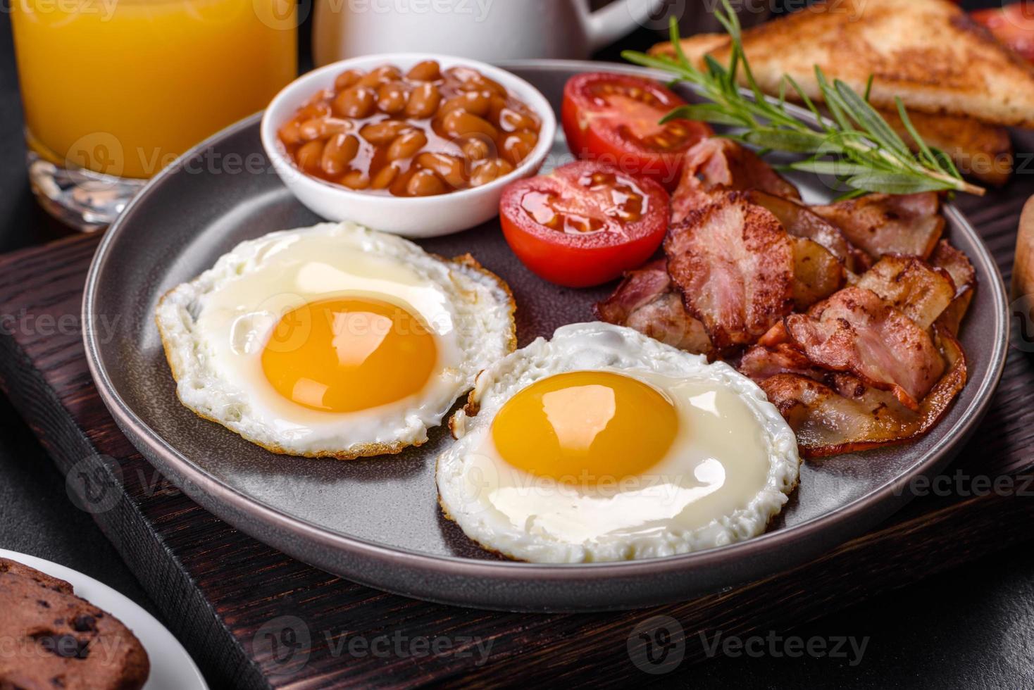 A delicious nutritious healthy breakfast with fried eggs, bacon, beans, a glass of juice, oat cookies, milk and jam photo