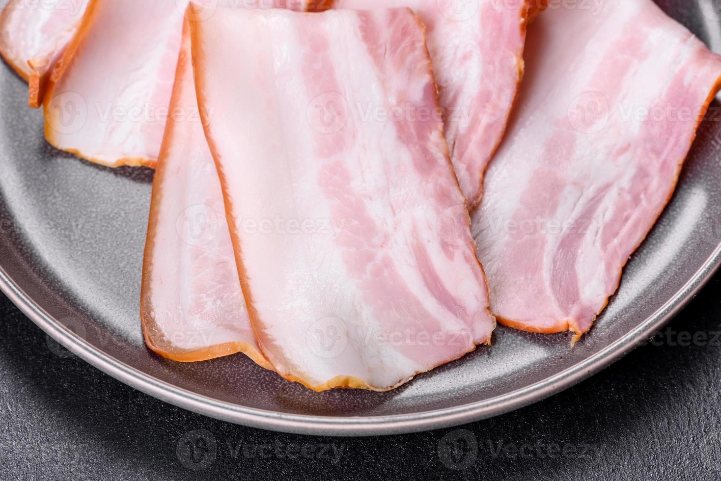 Delicious fresh raw bacon cut with slices on a grey plate against a dark concrete background photo