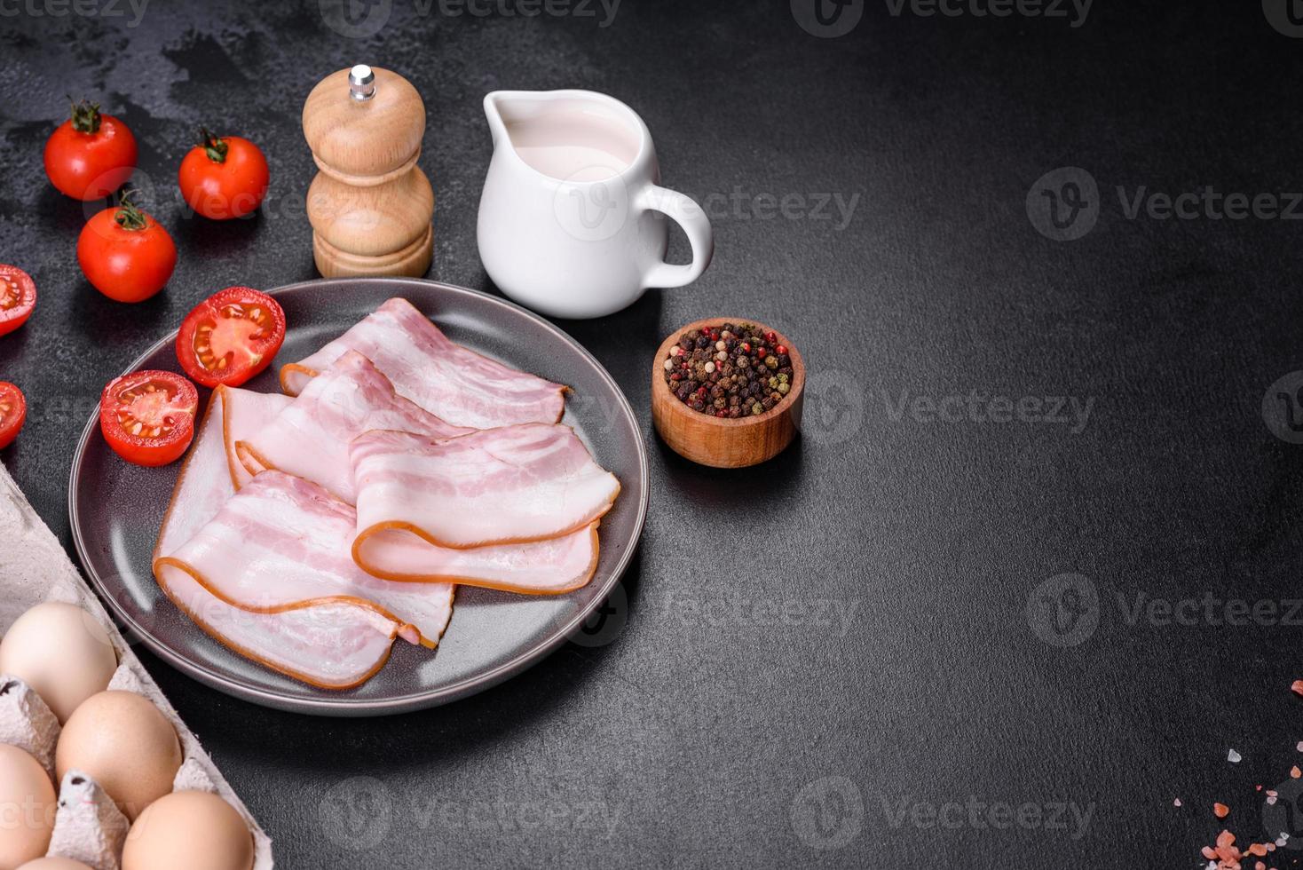 Delicious fresh raw bacon cut with slices on a grey plate against a dark concrete background photo