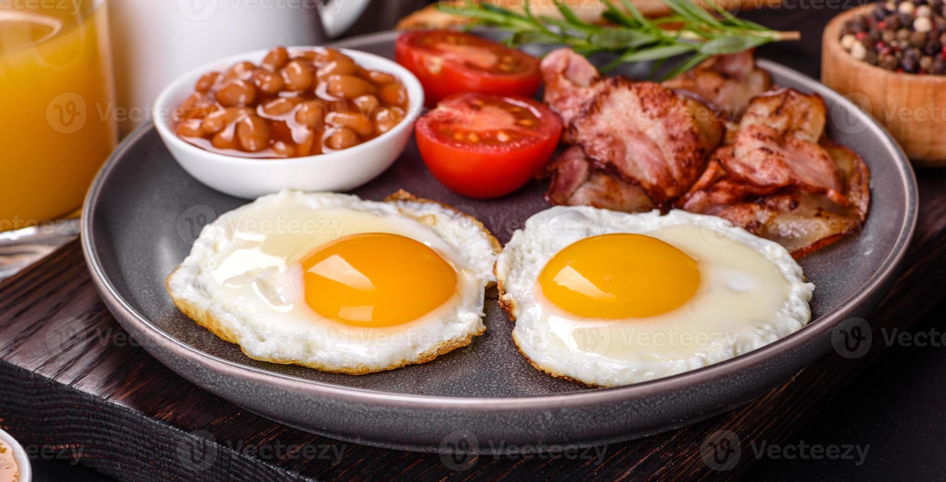 A delicious nutritious healthy breakfast with fried eggs, bacon, beans, a glass of juice, oat cookies, milk and jam photo