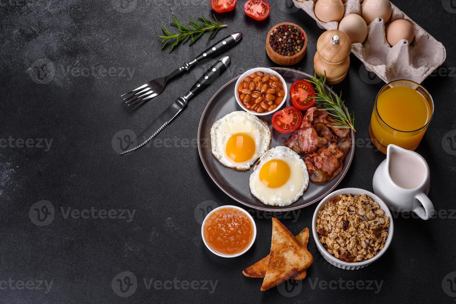 A delicious nutritious healthy breakfast with fried eggs, bacon, beans, a glass of juice, oat cookies, milk and jam photo