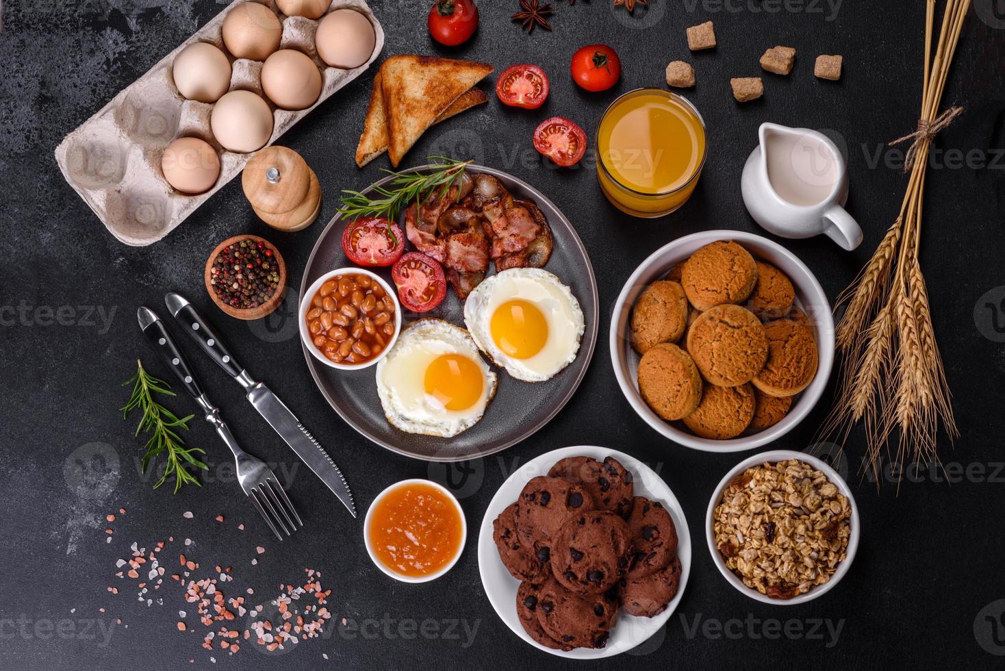 A delicious nutritious healthy breakfast with fried eggs, bacon, beans, a glass of juice, oat cookies, milk and jam photo