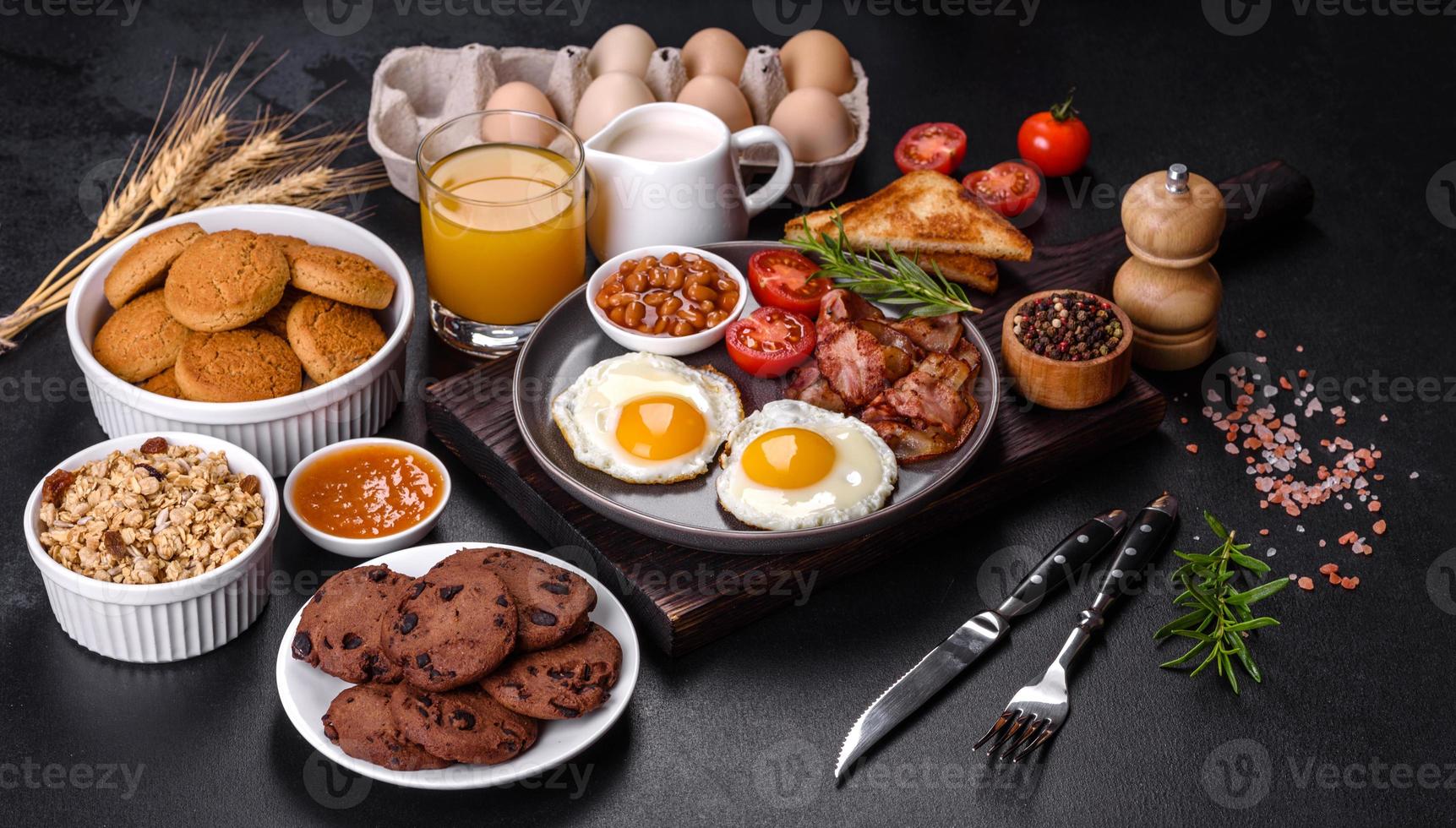 A delicious nutritious healthy breakfast with fried eggs, bacon, beans, a glass of juice, oat cookies, milk and jam photo