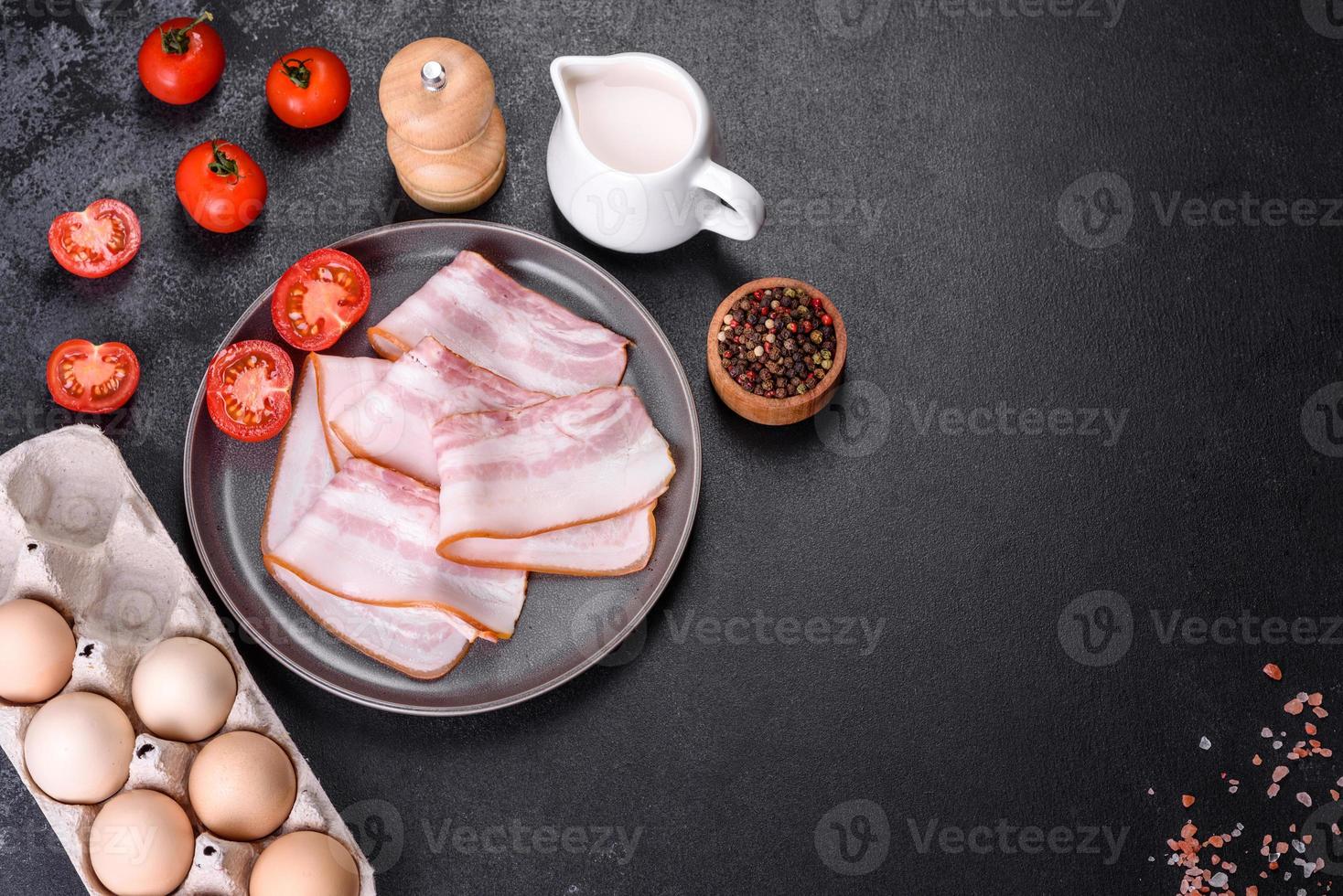 Delicious fresh raw bacon cut with slices on a grey plate against a dark concrete background photo