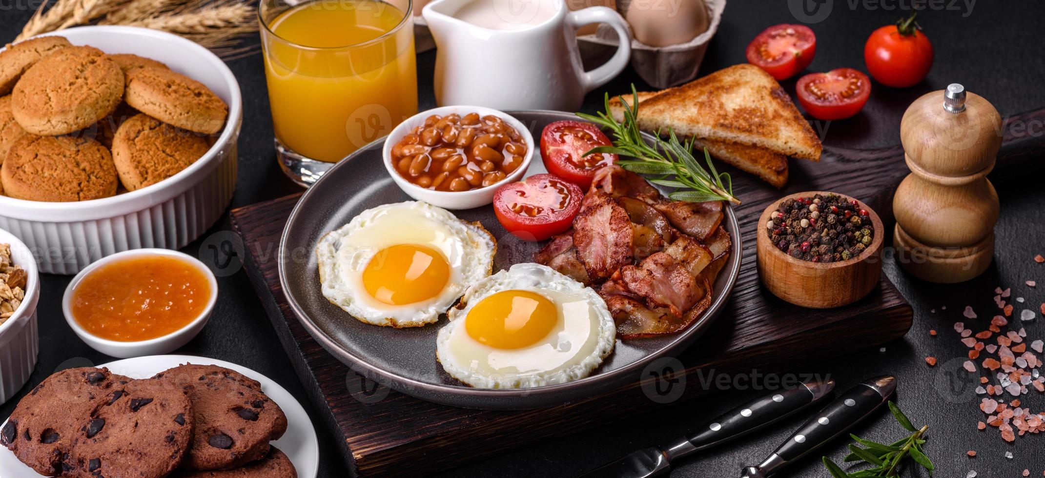 A delicious nutritious healthy breakfast with fried eggs, bacon, beans, a glass of juice, oat cookies, milk and jam photo