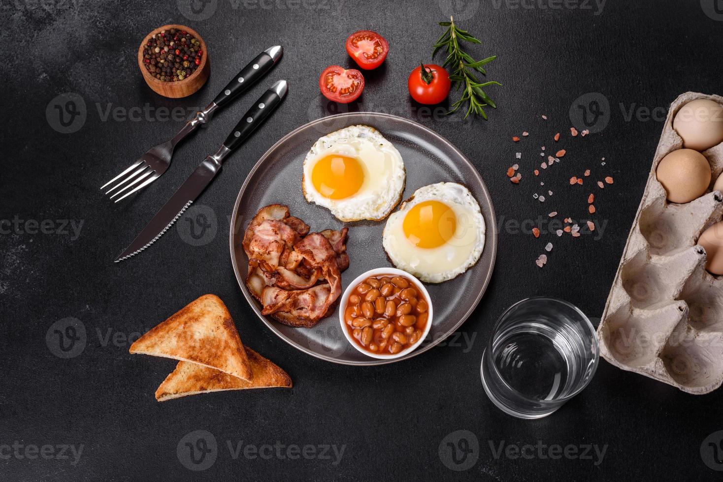 un delicioso desayuno saludable y nutritivo con huevos fritos, tocino, frijoles, un vaso de jugo, galletas de avena, leche y mermelada foto