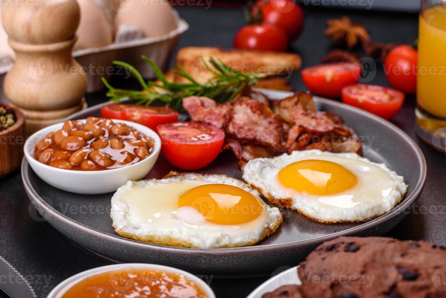 A delicious nutritious healthy breakfast with fried eggs, bacon, beans, a glass of juice, oat cookies, milk and jam photo