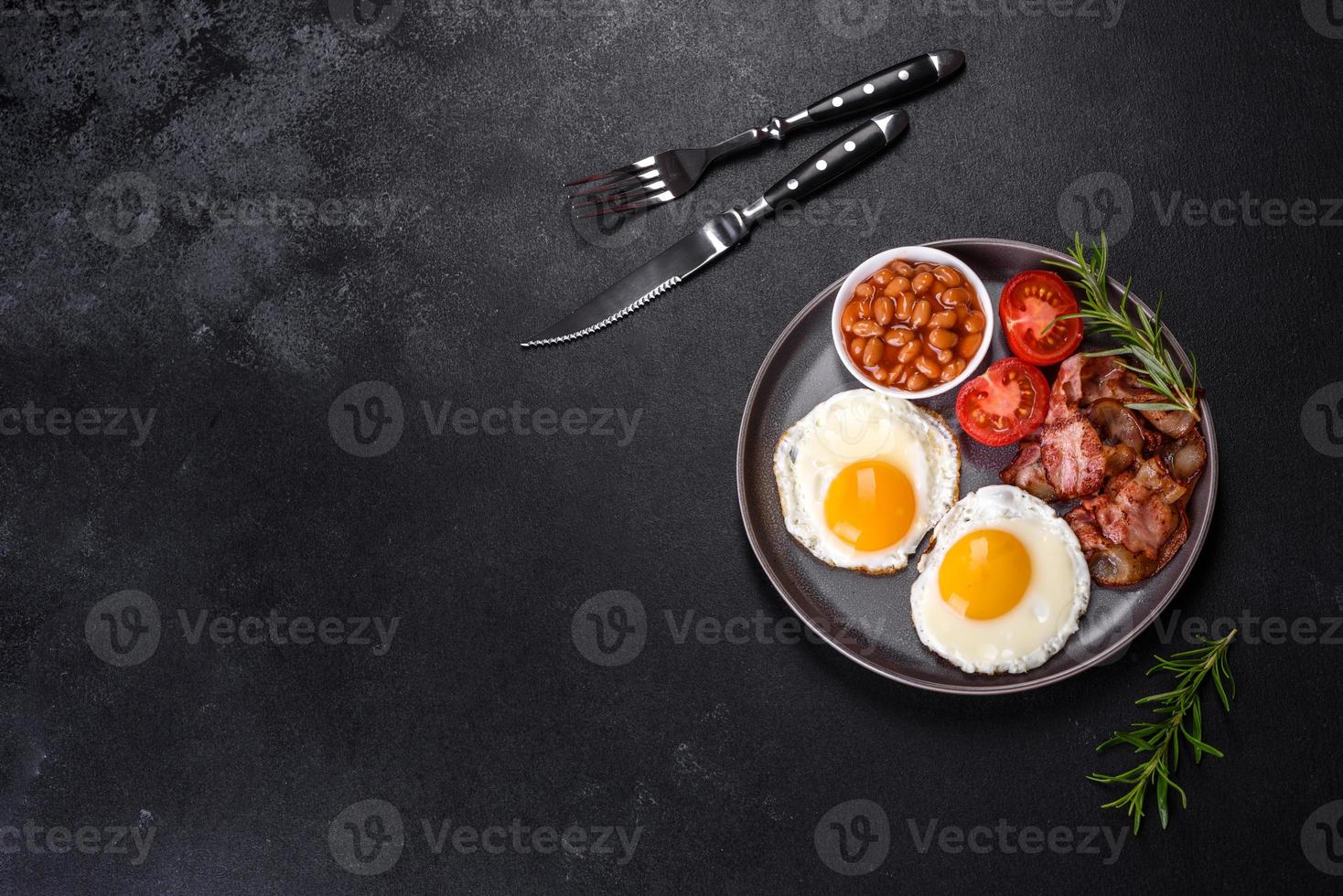 A delicious nutritious healthy breakfast with fried eggs, bacon, beans, a glass of juice, oat cookies, milk and jam photo