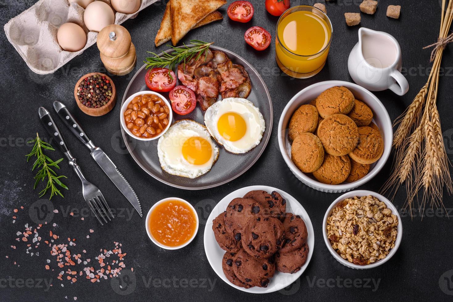 A delicious nutritious healthy breakfast with fried eggs, bacon, beans, a glass of juice, oat cookies, milk and jam photo